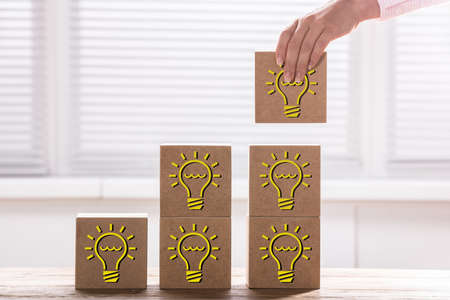 Woman's Hand Holding A Block With Light Bulb To Complete Growth Bar Graph On Deskの写真素材