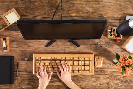 Elevated View Of A Businesswoman Using Wooden Keyboard In Front Of Computer On Office Deskの写真素材