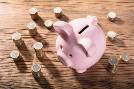 Elevated View Of A Piggybank Surrounded With Coin Stacks On Wooden Tableの写真素材