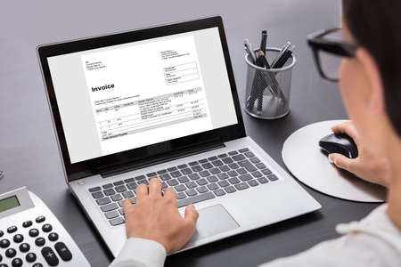 Close-up Of A Businesswoman Calculating Invoice On Laptop In Officeの写真素材