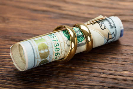 Golden Wedding Rings With Rolled Up Currency Note On Wooden Backgroundの写真素材