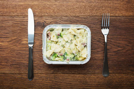 Elevated View Of A Pasta Meal In Foil Container With Fork And Knifeの写真素材