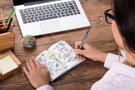 Close-up Of A Woman Drawing Start Up Business Plan On Notebook At Workplace