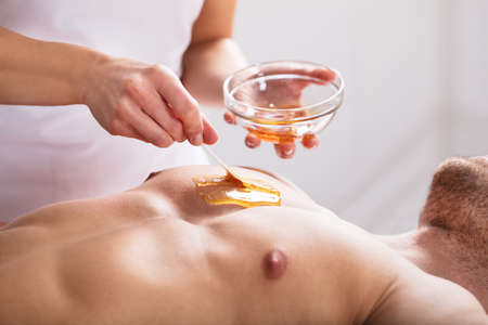 Close-up Of A Therapist Applying Wax On Man's Bodyの写真素材