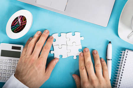 Elevated View Of A Businessperson Joining Puzzle On Office Desk At Work Placeの写真素材