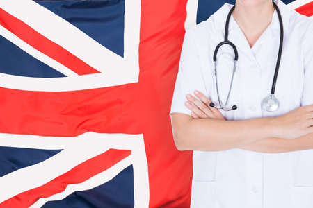 Close-up Of A Female Doctor With Folded Hands Standing Against British Flagの写真素材