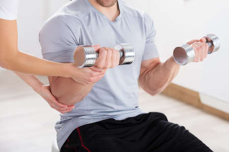 Close-up Of Instructor Assisting Man For Exercising With Dumbbellの写真素材
