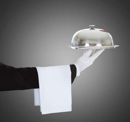 Close-up Of A Waiter's Hand Holding Cloche And Tray On Gray Backgroundの写真素材