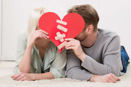 Couple Lying On Carpet Holding Paper Red Heart Fixed With Plaster Bandageの写真素材
