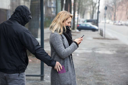 Man In A Hood Stealing Purse From Woman's Coat Pocket On Streetの写真素材
