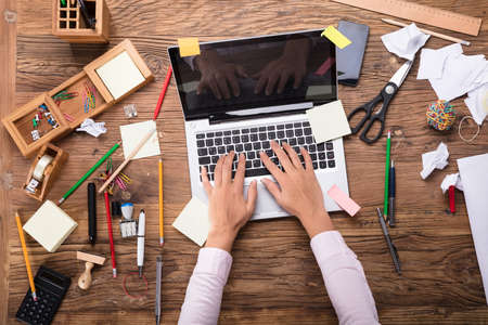Elevated View Of A Woman's Hand On Laptop At Messy Workplaceの写真素材