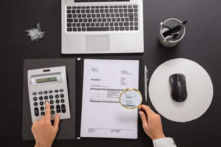 Close-up Of A Businesswoman Looking Invoice Through Magnifying Glass While Calculatingの写真素材