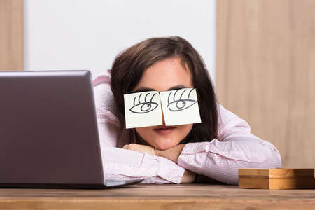 Sleeping Businesswoman Covering His Eyes With The Sticky Notes On Desk At Workplaceの写真素材
