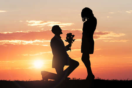 Silhouette Of A Man Proposing His Girlfriend Against Dramatic Sky At Sunsetの写真素材