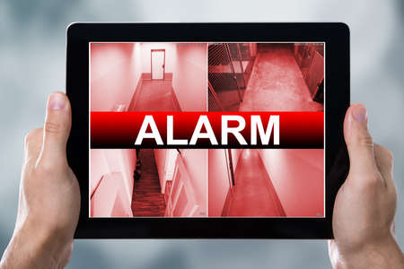 Close-up Of A Person With Digital Tablet Showing Alarm Text On Screenの写真素材