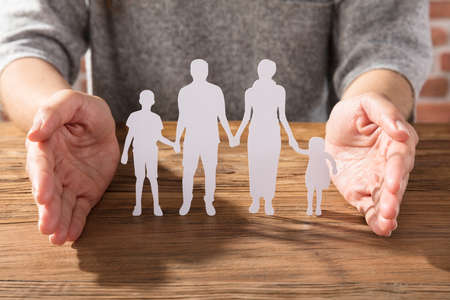 Close-up Of A Woman Protecting Family Of White Paper Cut Out On Wooden Deskの写真素材