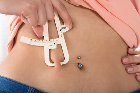 Woman Using Fat Caliper To Measure Body Fat On Waist Lineの写真素材