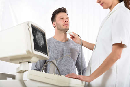 Young Man Getting Ultrasound Scan On Neck By Young Female Doctor In Clinic