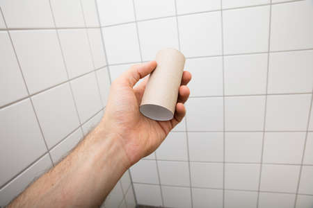Close-up Of A Man's Hand Holding Empty Toilet Paper Roll In Bathroomの写真素材