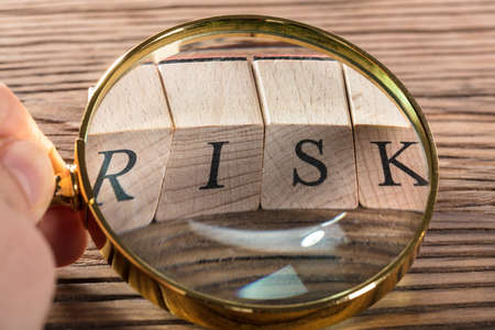 A Person Examining Risk Blocks Through Magnifying Glass On Wooden Tableの写真素材