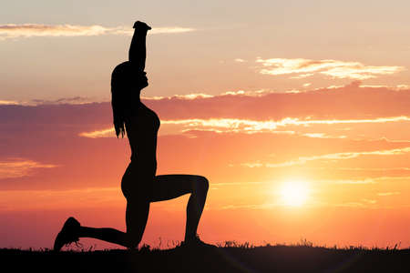 Silhouette Of A Woman Stretching Against Dramatic Sky At Sunsetの写真素材