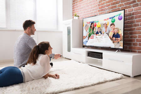 Young Couple Watching Party Celebration Video On Television At Home