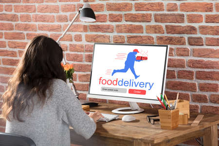 Rear View Of A Woman Ordering Food Online On Computer At Workplaceの写真素材