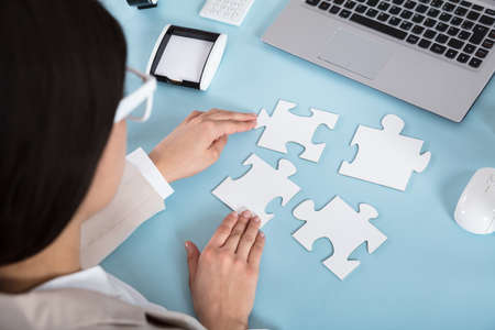 Businesswoman Trying To Join The Jigsaw Puzzle Pieces On Blue Desk