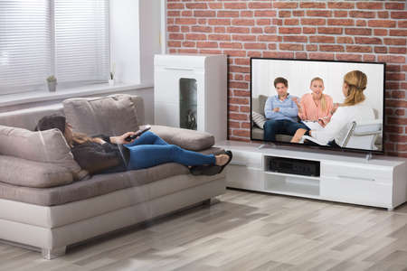 Young Woman Laying On Couch Watching Television At Home