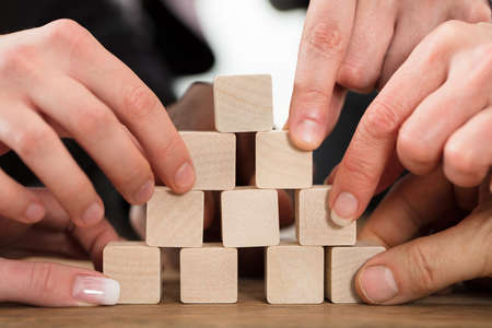Close-up Of A People Arranging Block On Pyramid Over The Wooden Tableの写真素材