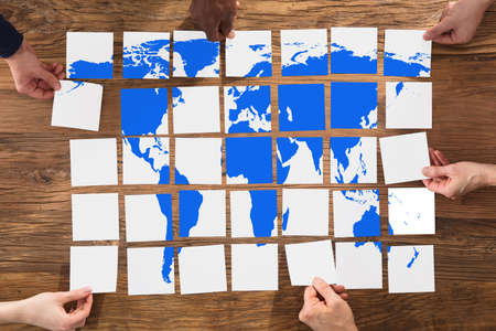 Hands Arranging The World Map Puzzle On Wooden Table