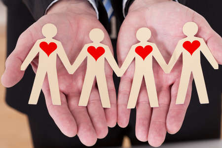 Close-up Of Man's Hand Showing Paper Cut Out Figures With Heart Shapeの写真素材