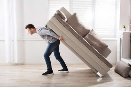 Young Man Trying To Move Sofa At Homeの写真素材