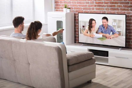 Rear View Of Couple Sitting On Couch Watching Television At Home