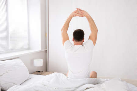 Rear View Of A Man Stretch His Hands After Waking Up In Bed At Morningの写真素材