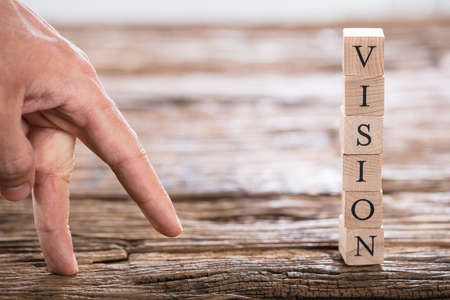 Close-up Of A Person's Finger And Stacked Vision Word On Wooden Blockの写真素材