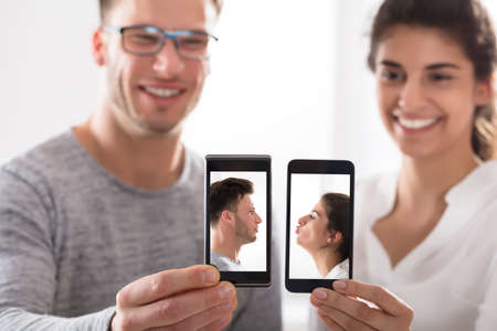 Smiling Young Couple Showing Their Cell Phone With Their Photos On Screenの写真素材