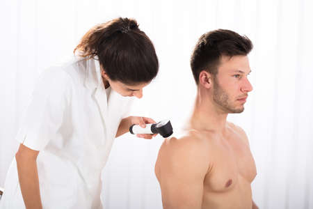 Close-up Of A Female Doctor Examining Skin Of Male Patient With Dermatoscopeの写真素材
