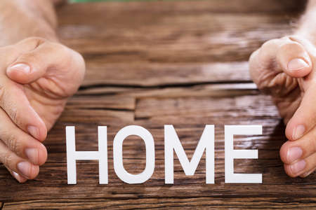 Close-up Of A Person Protecting Home Word On Wooden Table