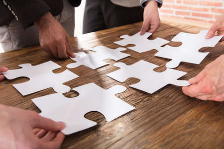 Group Of Businesspeople Arranging The Puzzle On Wooden Table