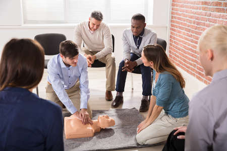 Young Male Instructor Showing CPR Training On Dummy To His Student