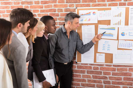 Business Colleague Looking At Graph Attached On Bulletin Board Over The Brick Wallの写真素材