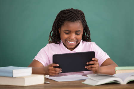 Schoolgirl Using Digital Tablet While Studying Against Chalkboardの写真素材