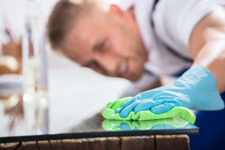 Close-up Of A Young Male Janitor Cleaning Desk With Green Clothの写真素材