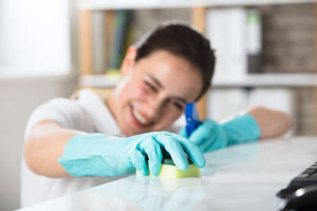 Smiling Young Woman Cleaning The Desk With Sponge In Office