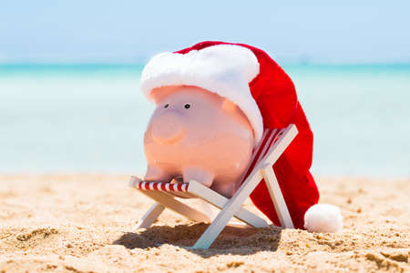 A Pink Piggy Bank With Santa Hat Kept On The Deck Chair At Beachの写真素材