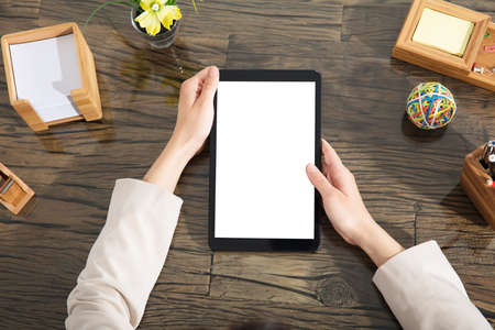 Close-up Of A Businessperson Holding Blank Digital Tablet Over The Wooden Desk