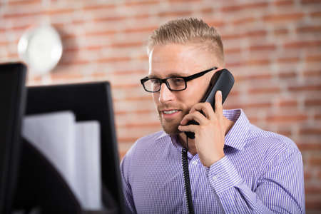 Portrait Of Young Businessman Talking On Phone At Officeの写真素材