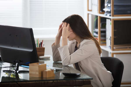 Young Businesswoman Suffering From Headache At Workplaceの写真素材
