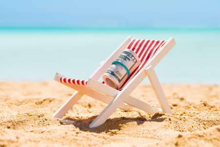 Rolled Up Bundle Of Fifty Dollar Banknotes On Miniature Deck Chair At Beachの写真素材